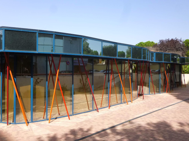 Ein modernes Schulgebäude mit zahlreichen Fenstern, einem vorderen Weg, der von Bäumen gesäumt ist, und einem klaren blauen Himmel.