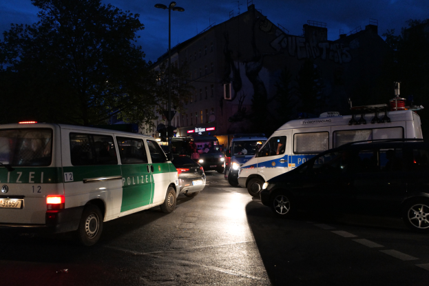 Eine Gruppe von Polizeiwagen, einschließlich eines Vans, eines Autos und eines Rades, parkte am Straßenrand in der Nacht, mit Gebäuden, Bäumen, Laternenmasten und einem sternenklaren Himmel im Hintergrund.