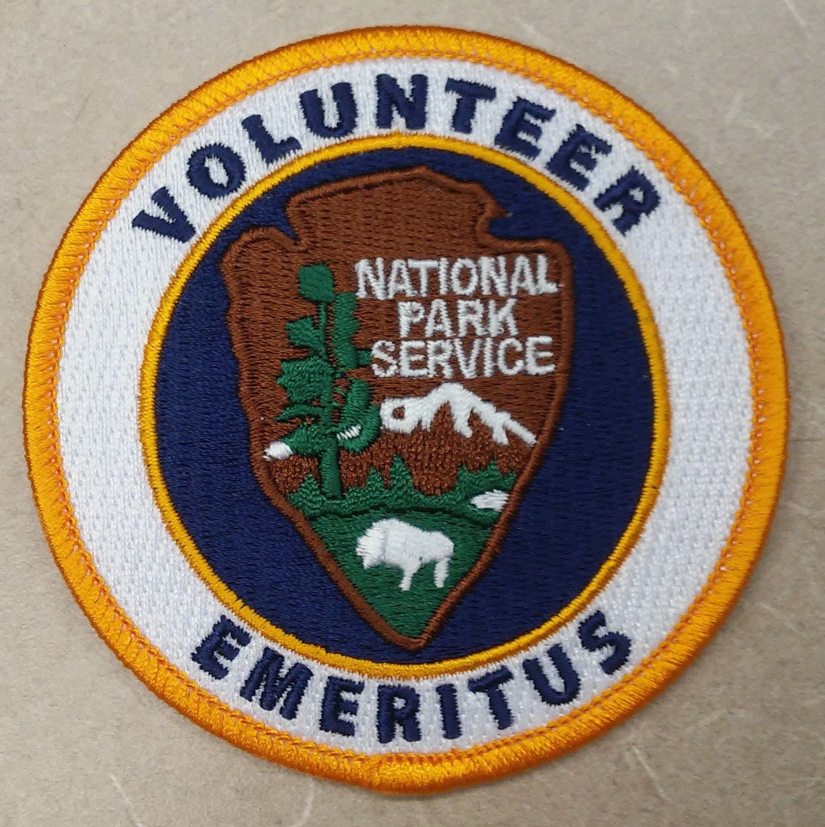 Runder Flicken mit "Volunteer National Park Service Emeritus" in fetter schwarzer Schrift auf weißem Hintergrund, umrandet von einem blauen Rand und einem gelben Kreis.