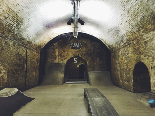 Skatepark mit Backstein-Tunnel, Rampe, Bank und beleuchteten Laternen, inklusive Texttafel.