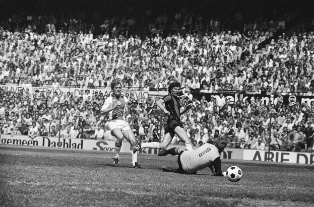 Schwarzes und weißes Foto von Füßballspielern im Einsatz auf einem Feld mit Zuschauern und einem Bundesliga 1978-79 Ajax 1-1 Hannover 96-Banner im Hintergrund.