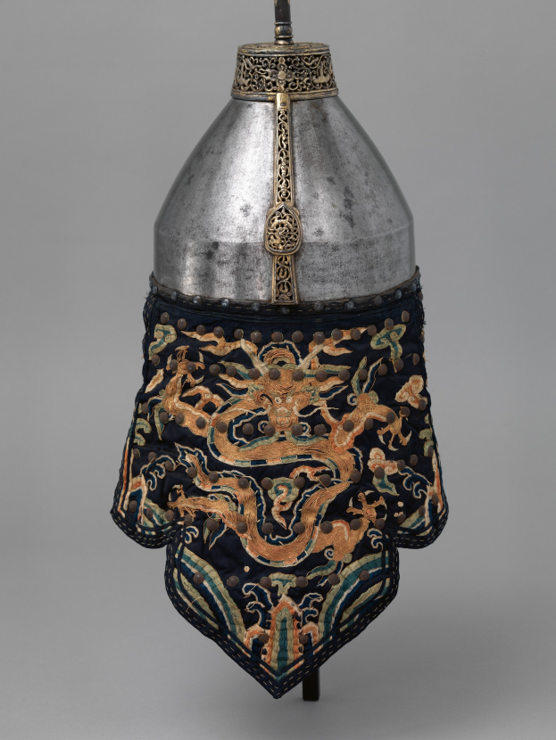 Metallhelm mit einer Drachengestaltung vor einem grauen Hintergrund, das detaillierte Metallarbeiten zeigt.