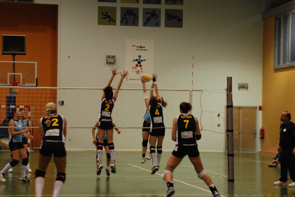 Ein Volleyballfeld mit aktiv spielenden Spielern, das einen Basketballkorb, Fenster und eine Tür im Hintergrund zeigt.