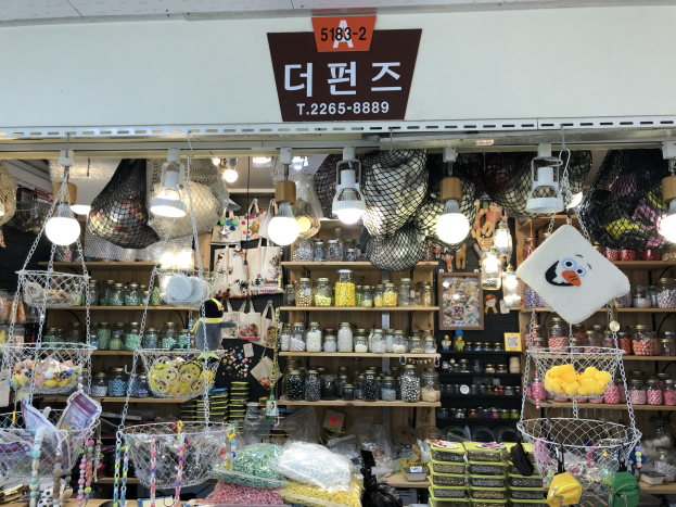 Ein unordentlicher Laden in Seoul, der verschiedene Gegenstände wie Körbe, Lichter, Flaschen und Spielzeuge auf Regalen ausstellt, mit einem Schild öber der Tür, das ihn als einen der besten koreanischen Läden ausweist.