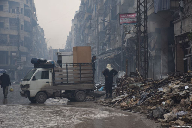 Eine beschädigte Straßenszene mit einem Lastwagen, Schutt, Passanten und Gebäuden, die den Einfluss des syrischen Bürgerkriegs widerspiegelt.