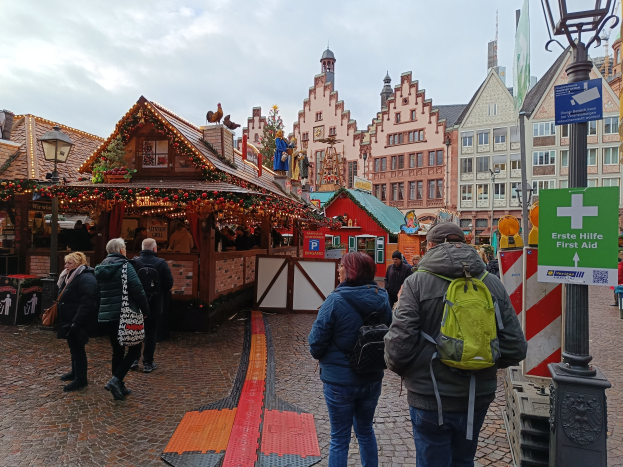 Menschen, die auf einem Kopfsteinpflasterweg neben einem Weihnachtsmarkt in Nürnberg, Deutschland, gehen, mit Laternenmasten, Texttafeln und Gebäuden im Hintergrund unter einem bewölkten Himmel.