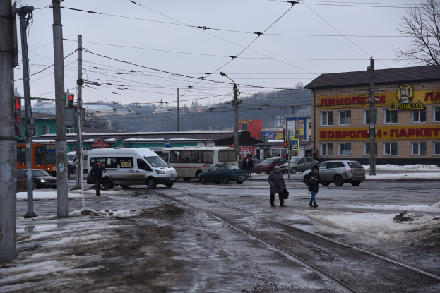 Gruppe von Menschen, die eine Straße neben einer Bahnschiene entlanggehen, mit Fahrzeugen, Strommasten, Laternen, Verkehrsampeln, Gebäuden, Bäumen und einem Van.