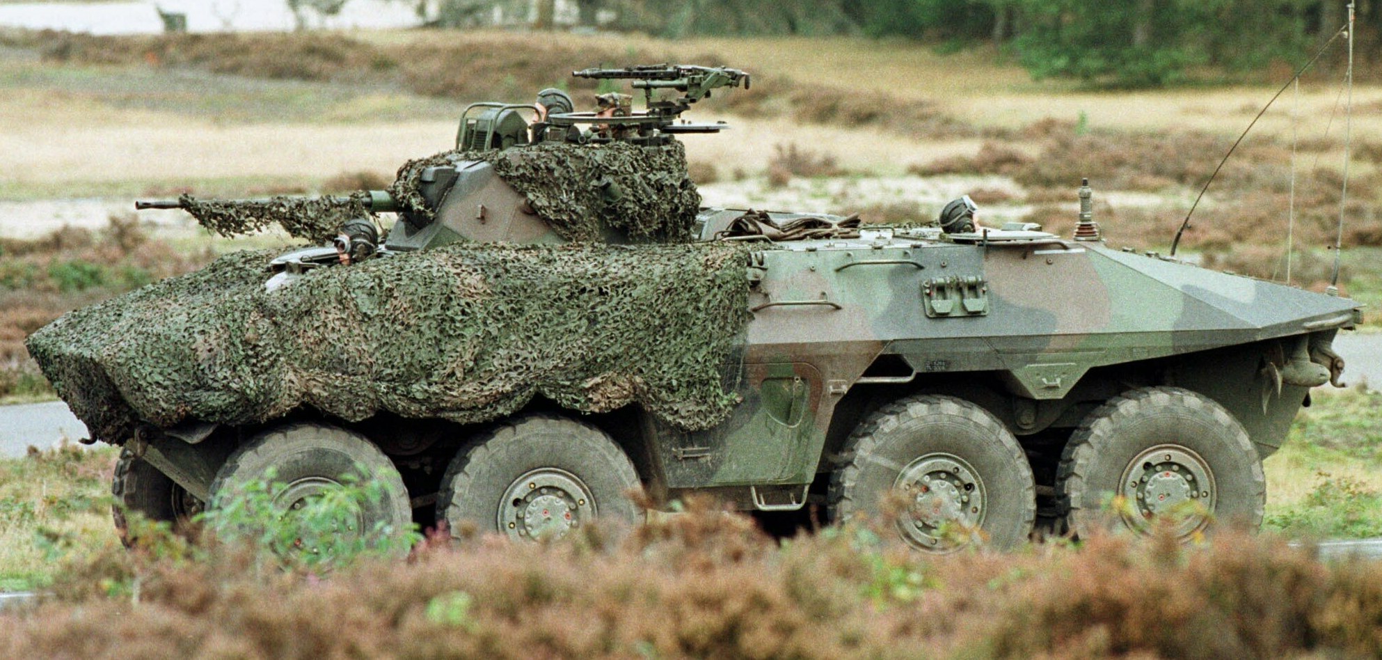Militärischer Personentransporter mit montierter großer Waffe fährt neben einer Waldstraße
