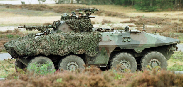 Militärischer Personentransporter mit montierter großer Waffe fährt neben einer Waldstraße