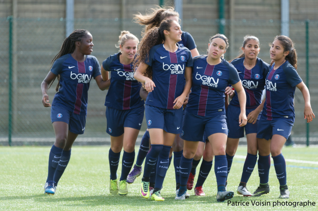 Gruppe junger Frauen beim Fußballspielen auf einem Rasenfeld mit Maschendrahtzaun, Pfosten und einer Wand im Hintergrund, mit dem Text "Paris Saint-Germain Women's Soccer" in der unteren rechten Ecke.