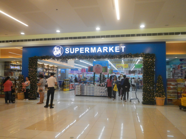 Gruppe von Menschen vor einem Supermarkt mit Einkaufstaschen, Einkaufswagen, Topfpflanze, Regalen, Schildern und Deckenleuchten.