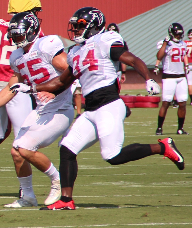 Eine Gruppe von Männern, die Fußball auf einem Feld mit einer Wand im Hintergrund spielen, alle mit Helmen und Fußballschuhen während eines Spiels.