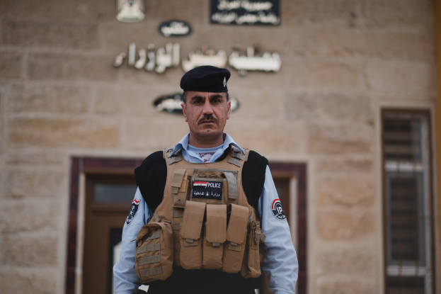 Polizist in Uniform vor einem Gebäude mit Türen, Fenstern und Text an der Wand.