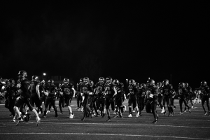 Schwarzes Bild von Fußballspielern in Helmen, die nachts auf das Feld laufen, mit Stadionlichtern und Pfosten im Hintergrund.