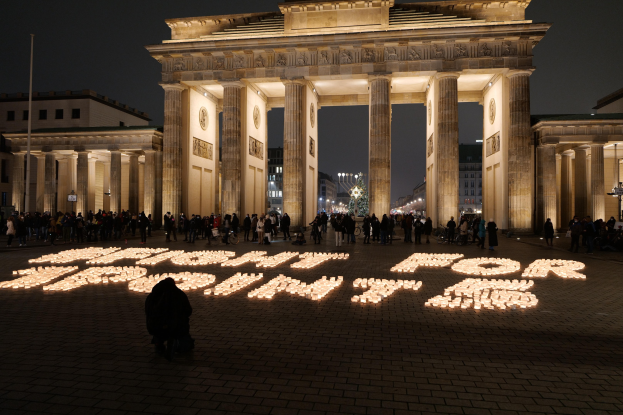 Eine Gruppe von Menschen steht vor dem beleuchteten Brandenburger Tor in Berlin, Deutschland, umgeben von Geb├Ąuden, Masten und Lichtern; die Worte 'Kampf für Freiheit' sind auf dem Boden zu sehen.