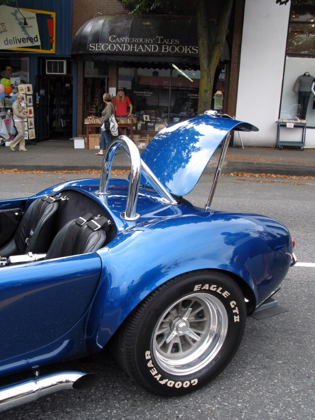Ein blaues Fahrzeug fährt auf einer Straße mit Geschäften und Menschen im Hintergrund.