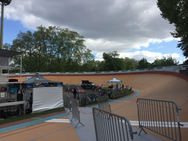 Gruppe von Radfahrern auf einer Schmutzspur bei den UCI BMX-Weltmeisterschaften 2018, mit Zelten, Fahrzeugen und Bäumen im Hintergrund.