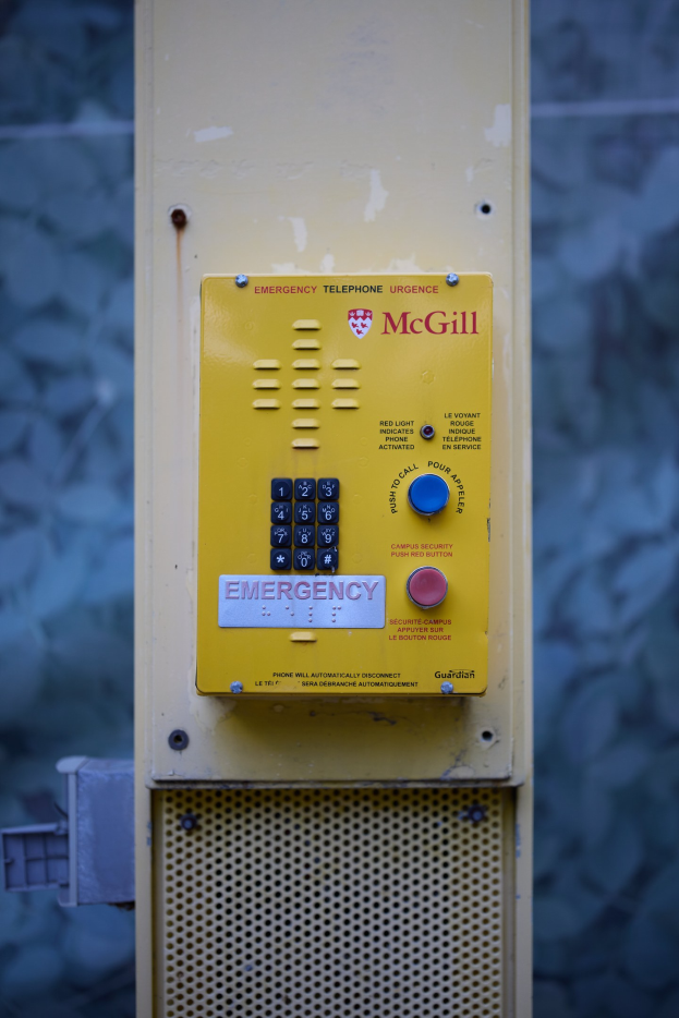 Ein gelbes Nottelefon an einer Gebäudeseite angebracht, mit Tasten und Text für Notrufe, vor einer Wand.