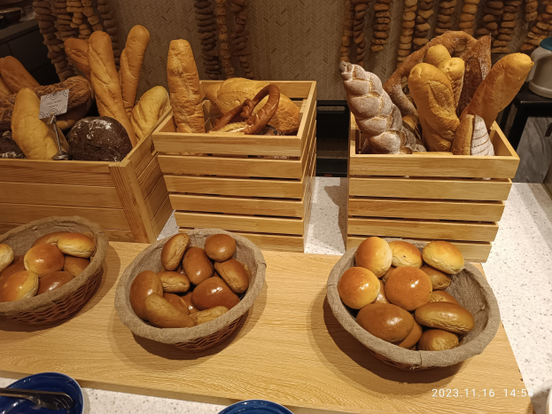 Ein Holztisch zeigt Körbe mit verschiedenen Brotsorten, Teller und Löffel, mit einer Wasserzeichenwand im Hintergrund eines Pariser Bäckerei.