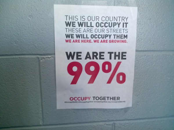 Schwarzes Plakat an einer Wand mit fetter Schrift, die "Occupy Wall Street" und "Wir sind die 99%." lautet.