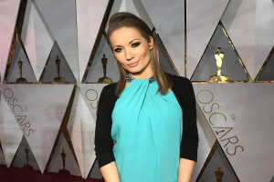 Frau in einem blauen und schwarzen Kleid auf einem roten Teppich bei der Oscar-Verleihung 2018 - Ankunft auf dem roten Teppich, mit einer Tafel, die den Veranstaltungsnamen und abstrakte Skulpturen im Hintergrund anzeigt.
