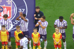 Gruppe junger Jungs auf einem Fußballfeld, die klatschen, mit einem Banner und Logos im Hintergrund.