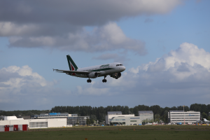 Ein Alitalia Airbus A330-300 startet vom Frankfurter Flughafen, mit Gras darunter, Gebäuden und Bäumen im Hintergrund und Wolken am Himmel.