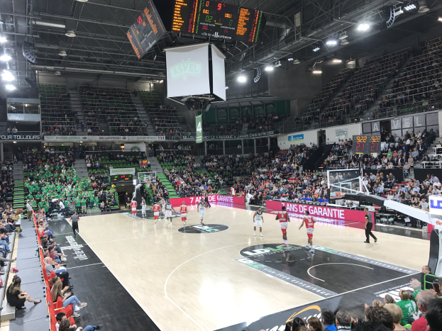 Ein Basketballspiel zwischen Asvel und Galatasaray wird in einer großen Arena mit Zuschauern und Texttafeln um den Platz herum gespielt.