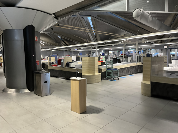 Ein geräumiger Raum im neuen Terminal des Frankfurter Flughafens, gefüllt mit Tischen, Stühlen, Maschinen, Säulen und Lampen, mit einigen wenigen Menschen und der Decke sichtbar.