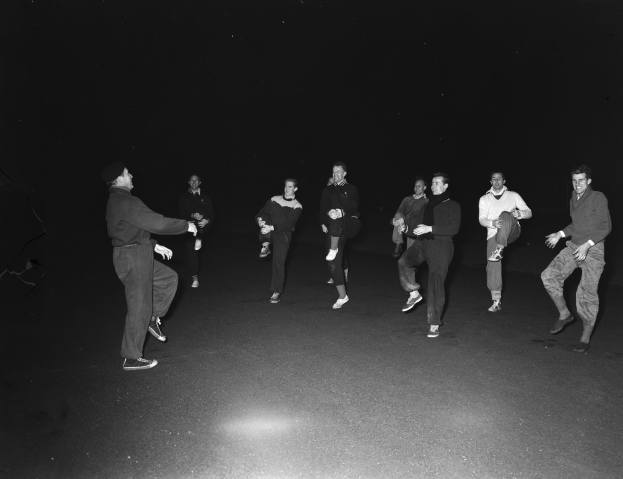 Eine Gruppe von Männern in Schuhen auf einer Bühne in einem Schwarz-Weiß-Setting, was eine Vorstellung suggeriert.