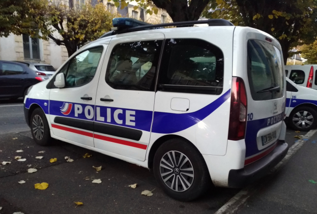 Ein Polizeiwagen parkt auf einer Straße, die von Gebäuden, Bäumen und verstreuten Blättern gesäumt ist.