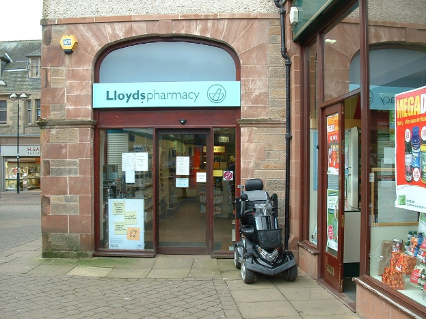 Apothekenladen mit einem Fahrzeug davor und einem Gebäude in der linken Ecke.